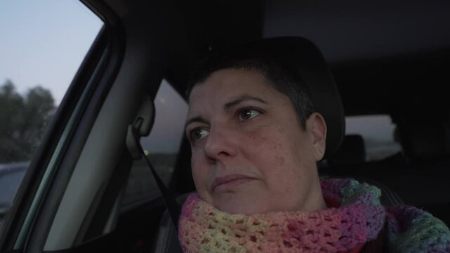 video of woman in car looking out of window, looking sad and pensive. Wearing a colourful scarf