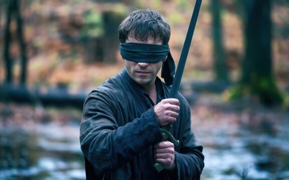 A person holding a sword stands in a forest, dressed in a dark robe, surrounded by autumn foliage and a serene landscape.