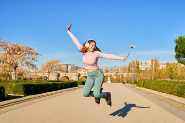 Young sporty woman jumping with inline skates and headphones in a park