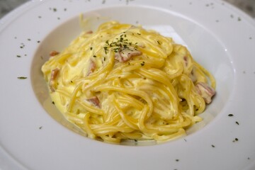 Creamy spaghetti carbonara served on a white plate, garnished with herbs and featuring a rich cheese sauce with bacon, close up and high angle view