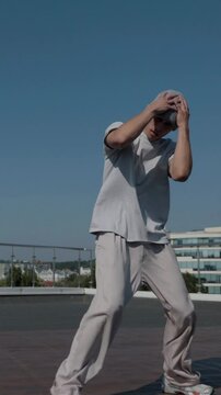 Vertical. The guy coolly dances breakdance on the roof of the house. A man dances an energetic athletic dance. Man effortlessly break dancing on a rooftop. Urban dancer showing off skills on rooftop. 