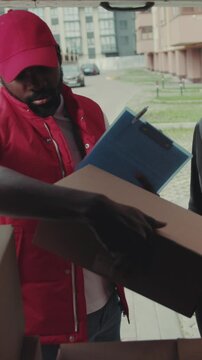 Courier African American gives a parce to a woman after signing on delivery device cardboard technology box order post postal service device sunny beard covered load logistic mailman