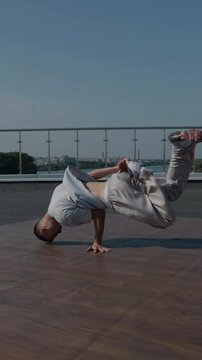 Vertical. The guy coolly dances breakdance on the roof of the house. A man dances an energetic athletic dance. Man effortlessly break dancing on a rooftop. Urban dancer showing off skills on rooftop. 
