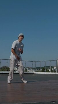 Vertical. The guy coolly dances breakdance on the roof of the house. A man dances an energetic athletic dance. Man effortlessly break dancing on a rooftop. Urban dancer showing off skills on rooftop. 