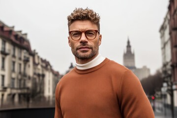 Stylish man with glasses stands confidently outdoors in urban environment on a cloudy day in a bustling city center