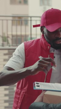 Close up face courier African American gives a parce to a woman after signing on delivery device cardboard technology box order post postal service device sunny beard covered load logistic mailman