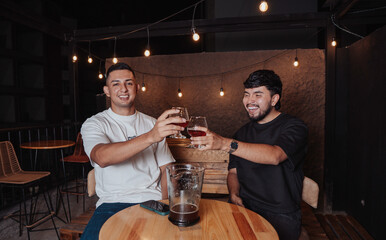 friends clinking their beer glass while smiling for the camera in a bar