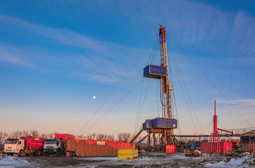 Industrial winter landscape featuring an operational drilling rig with support facilities at a...