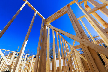 Wooden framework is beams being constructed for new house with clear skies sunlight illuminating