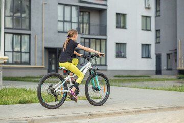 Preteen girl riding a bicycle in urban environment on a sunny day. Back view