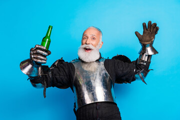 Senior man in medieval knight costume celebrating with a drink, cheerful gesture, blue background