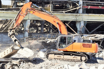 a modern powerful excavator cleans the rubble of a ruined building