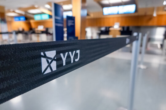 Victoria, British Columbia, Canada. Feb 11, 2025. A black retractable belt barrier with YYJ in white letters stands in a clean, modern airport terminal. Seating and large windows are visible in the BG