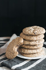 A plate of gluten-free chocolate chip cookies stacked neatly, with one cookie showing a bite taken out, placed on a striped cloth against a dark background