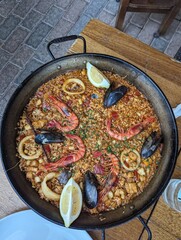 A pan of paella with shrimp, mussels, and lemon on a table