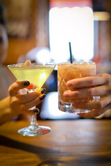  Close-up of two glasses of martini cocktail in female and male hand's