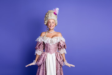 Graceful young woman in a baroque gown standing against a solid purple background, expressing elegance