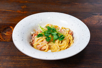 Delicious carbonara served in a white bowl on wooden table