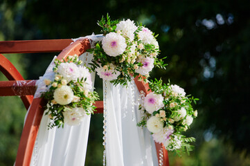 Elegant Wedding Arch Decorated with Flowers and Draped White Fabric Outdoors..