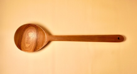 One brown wooden spoon kitchen utensil isolated on horizontal yellow cream colored background.