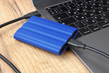 Blue external drive connected to a laptop on wooden desk.