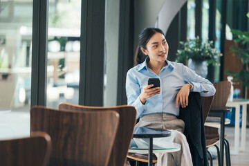 Young Asian professional working remotely, checking smartphone during break in sunlit contemporary...