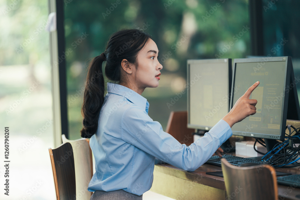 Poster Professional businesswoman pointing at computer monitor while analyzing data, working intently within sleek corporate workspace representing career success