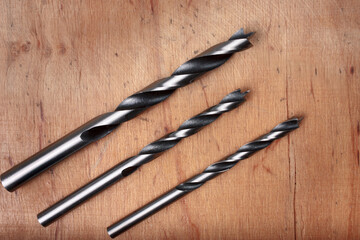 Three metal drill bits on a wooden surface.