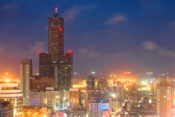 Obraz premium Nightscape of Kaohsiung City, a vibrant seaport in South Taiwan, with the landmark 85 Sky Tower standing among modern buildings, street lights dazzling in blue twilight and ships parking in the harbor