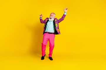 Photo of eccentric positive cool senior man dressed stylish bright clothes dance empty space isolated on yellow color background
