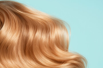 Fototapeta premium Golden Waves: Long, flowing blonde hair cascades in luxurious waves against a light blue background, showcasing its shine, health, and vibrant color. 