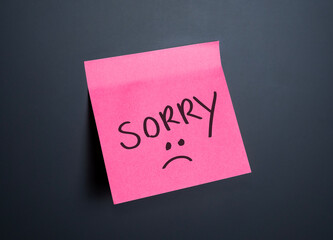 Apology note on a pink sticky pad with a sad face