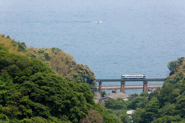 A local train traveling on Honmura Bridge of Yosan Railway Line along a beautiful coastline and a fishing boat navigating in blue Seto Inland Sea in the background, in Matsuyama, Ehime, Shikoku, Japan