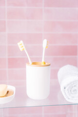 Two yellow toothbrushes in holder in bathroom on pink background.