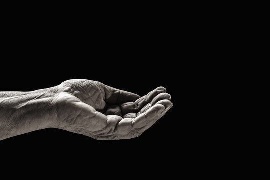 Old man hand on a black background. Old lady's hand with open palm. Elderly lady is waiting for help. Elderly woman, wrinkled hand palm reaching out forward. Black and white