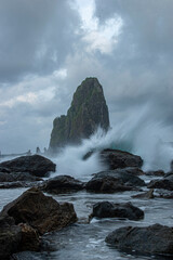 Long exposure of waves crashing rocks at the beach with an islet in the background.