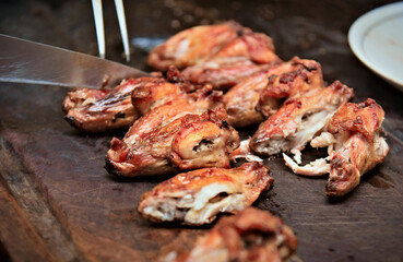 Marinated chickens grilled on a barbecue being prepared on a wooden surface