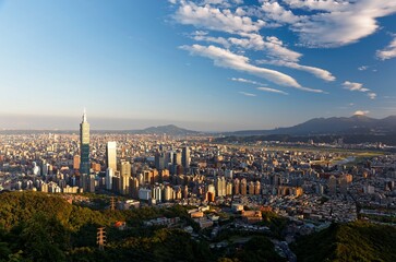 Aerial view of Taipei at dusk, the capital city of Taiwan, with 101 Tower standing out in Xinyi Commercial District, ovoid shaped Taipei Dome in nearby area and Tamsui River winding under golden sky
