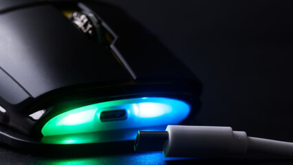 USB type-c charging of a modern wireless gaming computer mouse with bright LED lights in a dark environment. Photo. Selective focus. Close-up © slexp880