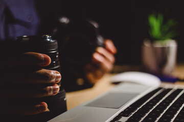 Professional photographer working on laptop, camera lens nearby, dim office lighting, small plant softening industrial workspace at night