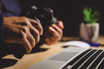 Skilled photographer working at desk, laptop nearby, transferring digital images from camera, focused on post production editing after professional photoshoot