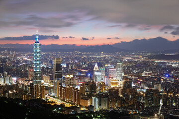 Fototapeta premium Aerial panorama of Taipei City, the vibrant capital of Taiwan, with the landmark 101 Tower standing in Xinyi Commercial District & Tamsui River winding by distant mountains under dramatic sunset sky