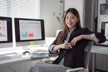 Young beautiful Asian businesswoman analyzing marketing data on computer screen while sitting at desk and working on financial accounting and investment advisor consulting