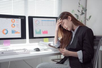 Young Asian businesswoman is having a bad headache while working on a difficult task, analyzing...