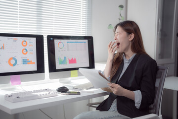 Businesswoman yawning while reading a report in her office, reflecting signs of tiredness and boredom from long hours of work and the pressures of looming deadlines