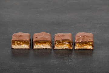 Candy bar with nougat, caramel, peanuts and hazelnuts. In chocolate. Dark gray background