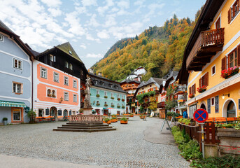 Scenic view of the old town square of Hallstatt, with a statue in the center, traditional colorful houses around the paved square, and fall mountains in background in Salzkammergut region of Austria