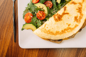 Tortilla with champignons with salad in a square white plate.