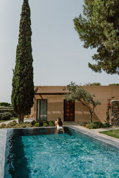 A woman in a swimsuit relaxes in a luxurious outdoor pool, surrounded by lush greenery and olive trees. A serene escape into nature perfect for wellness tranquility and self care moments in Greece
