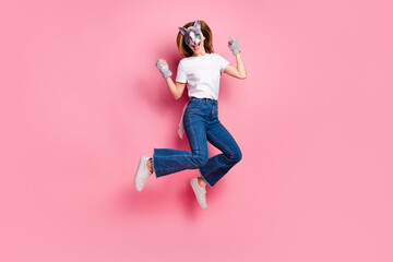Young woman in a cute cat mask jumping joyfully against a bright pink backdrop, expressing lively...
